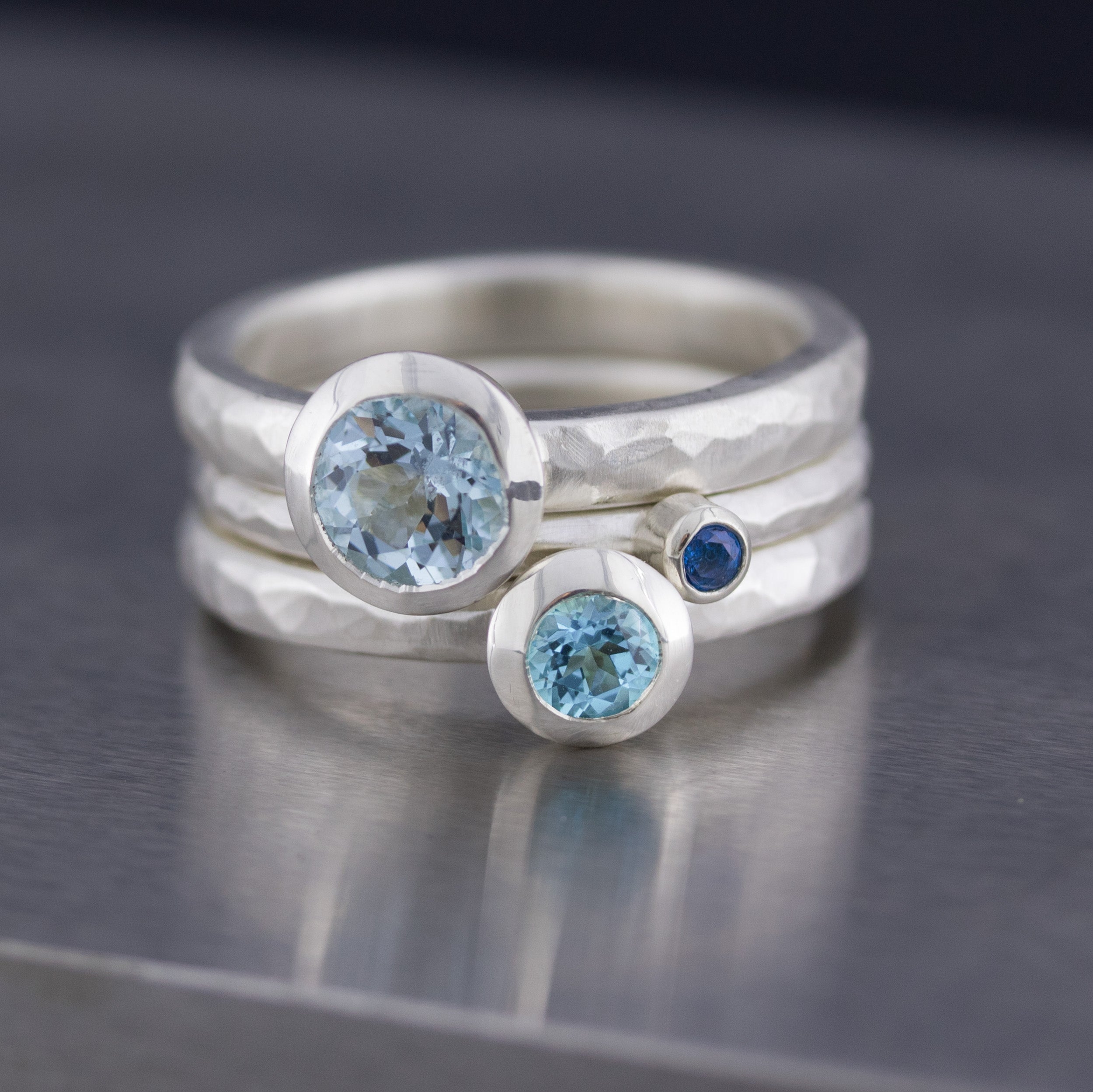 Ringset mit Topas, blau. 3 Silberringe mit geschmiedeten Oberflächen. Die Ringe liegen auf einem Stahlamboss.