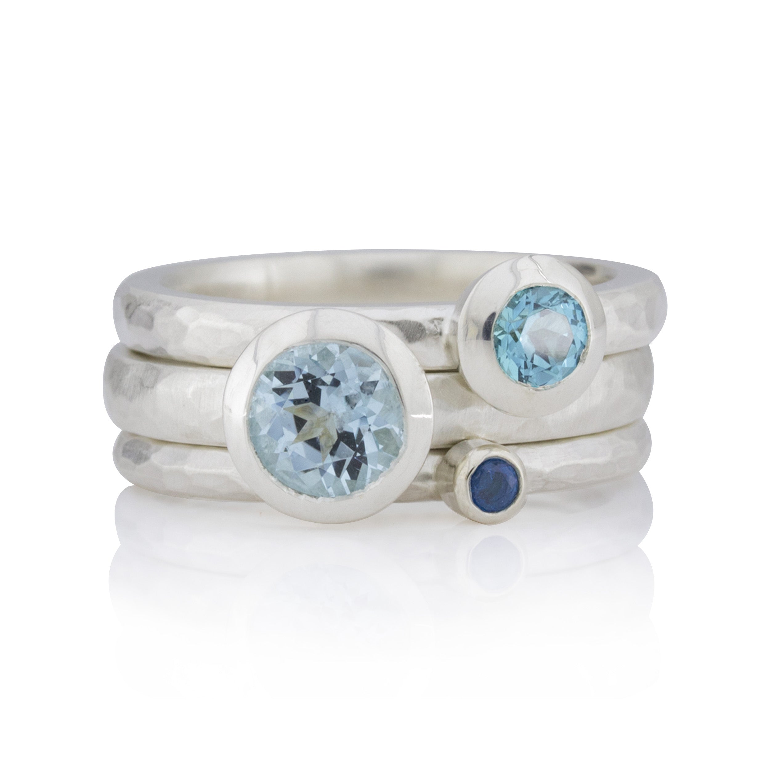 Ringset bestehend aus 3 Ringen. Alle Ringe haben geschmiedete Oberflächen. Ein Ring mit einem kleinen dunkelblauen Topas, ein Ring mit einem Blautopas mit einem Durchmesser von 6 mm, ein dritter Ring mit einem mittelblauen Topas und einem Durchmesser von 4 mm.