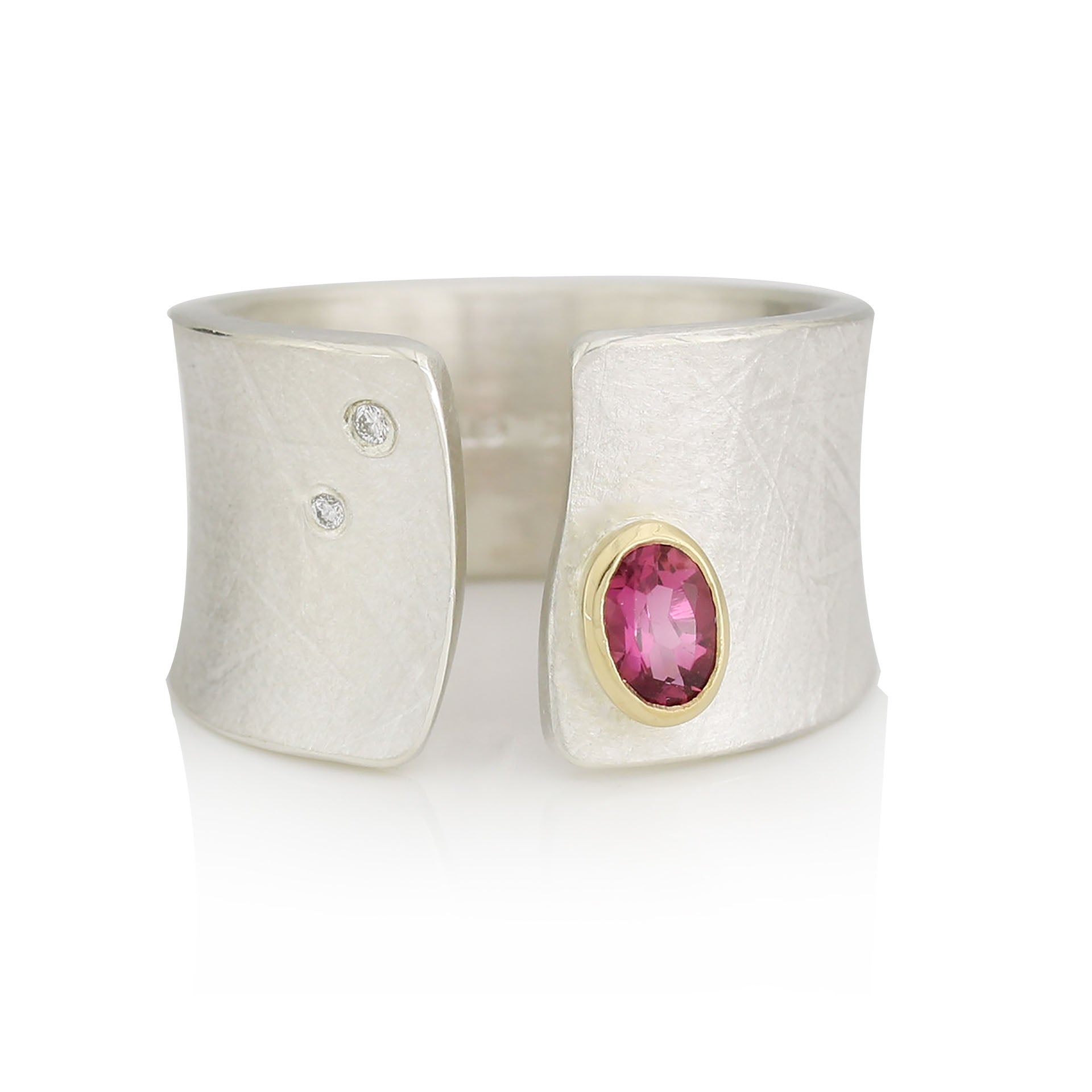 Breiter Silberring mit Turmalin, pink. Der Edelstein ist in eine Gelbgoldfassung eingefasst. Zwei kleine Diamanten sind auf der gegenüberliegenden Seite eingefasst. Zwischen den Steinen liegt eine organisch geformte Aussparung.