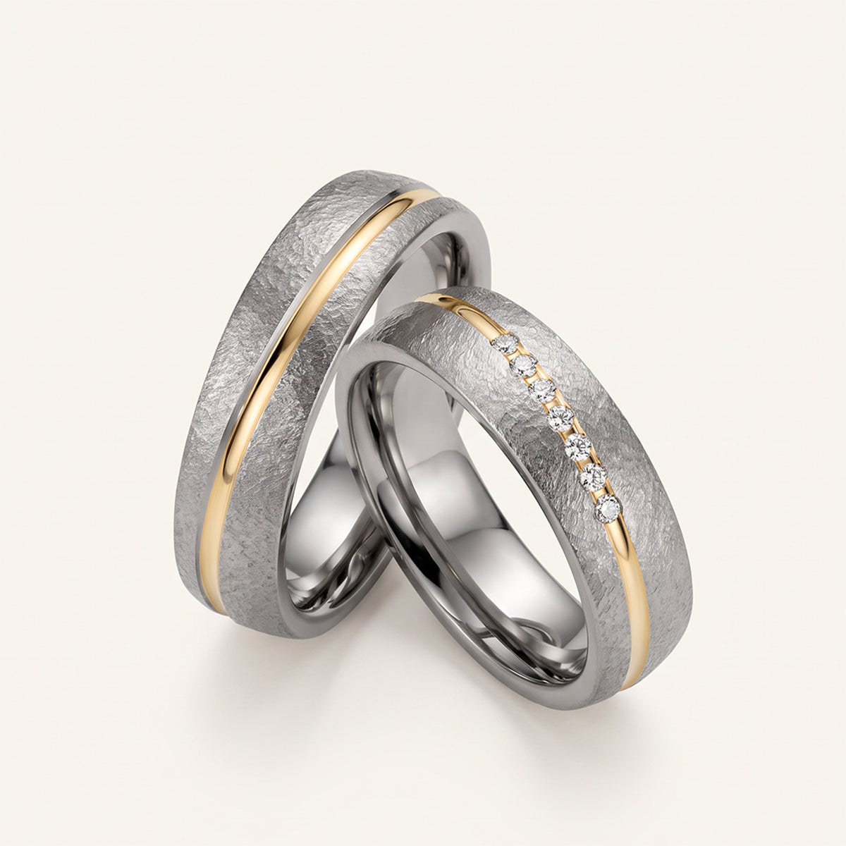 Trauringe aus Tantal mit einem eingelegten Gelbgoldband und Diamanten auf hellem Untergrund